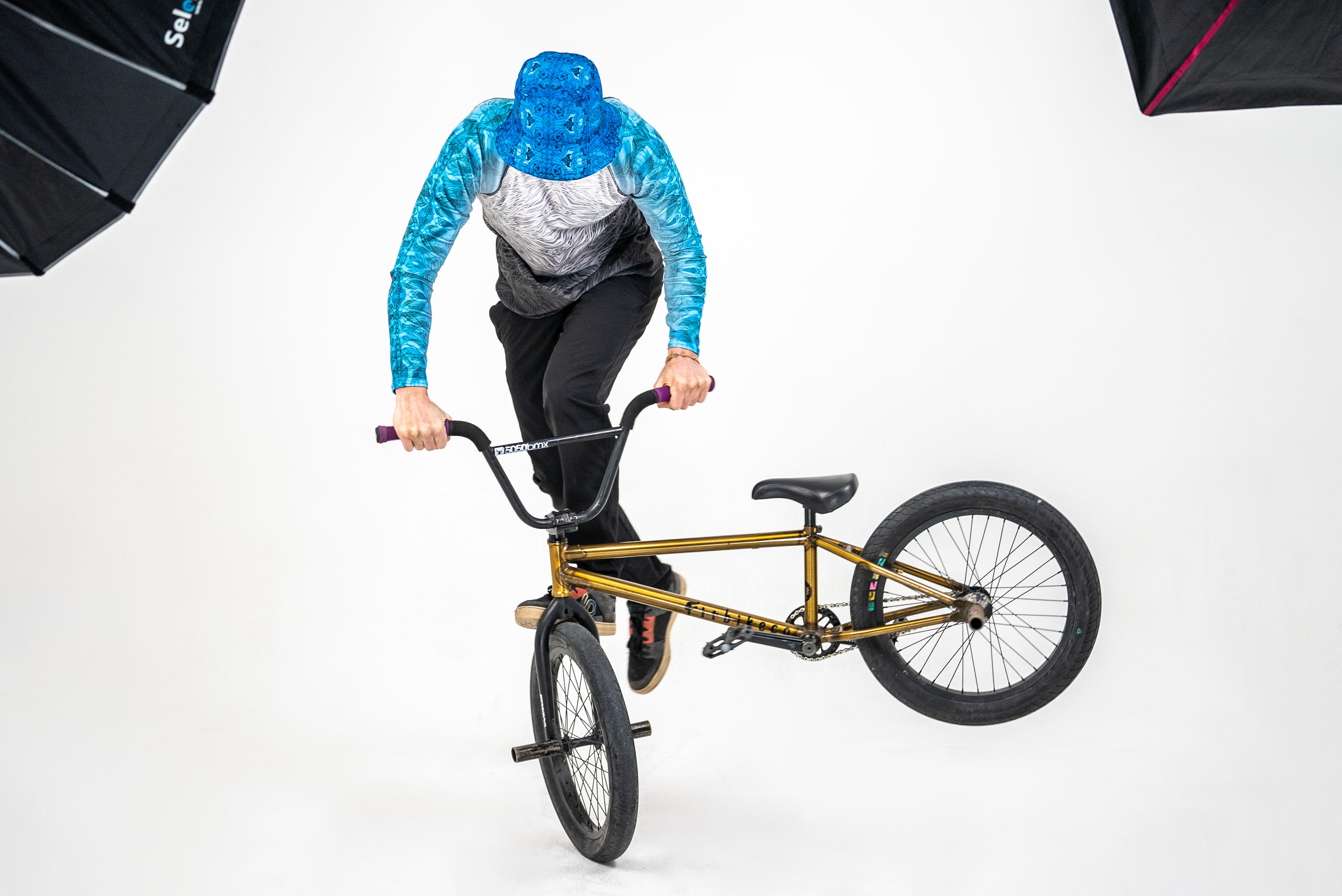 Model doing a trick on a bike and wearing a blue rash guard and bucket hat.