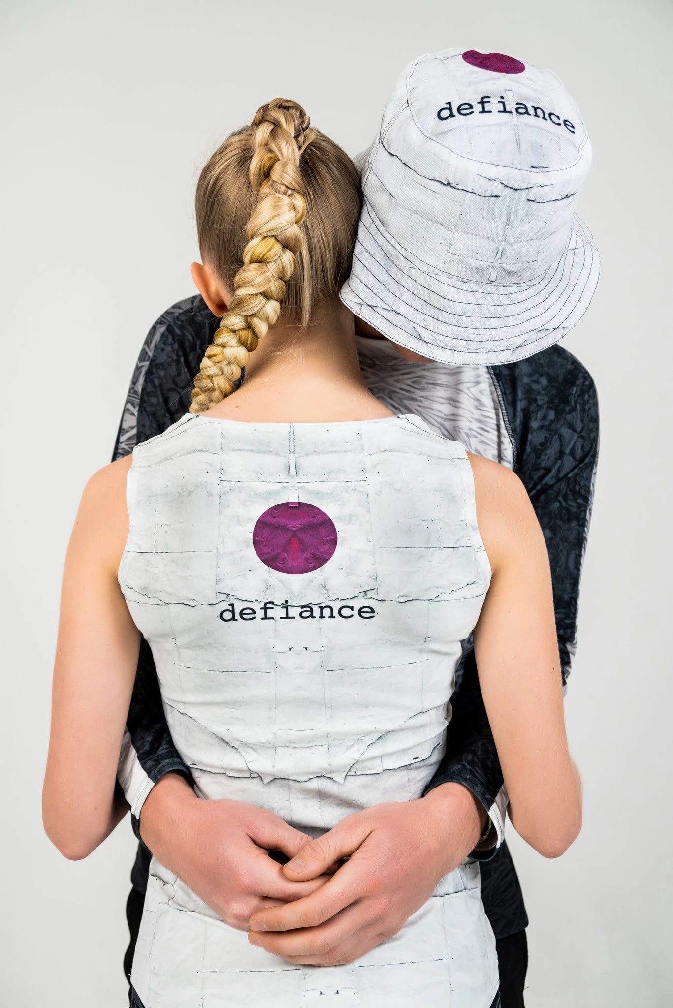 Models hugging, featuring a tank top and bucket hat with the Defiance logo.