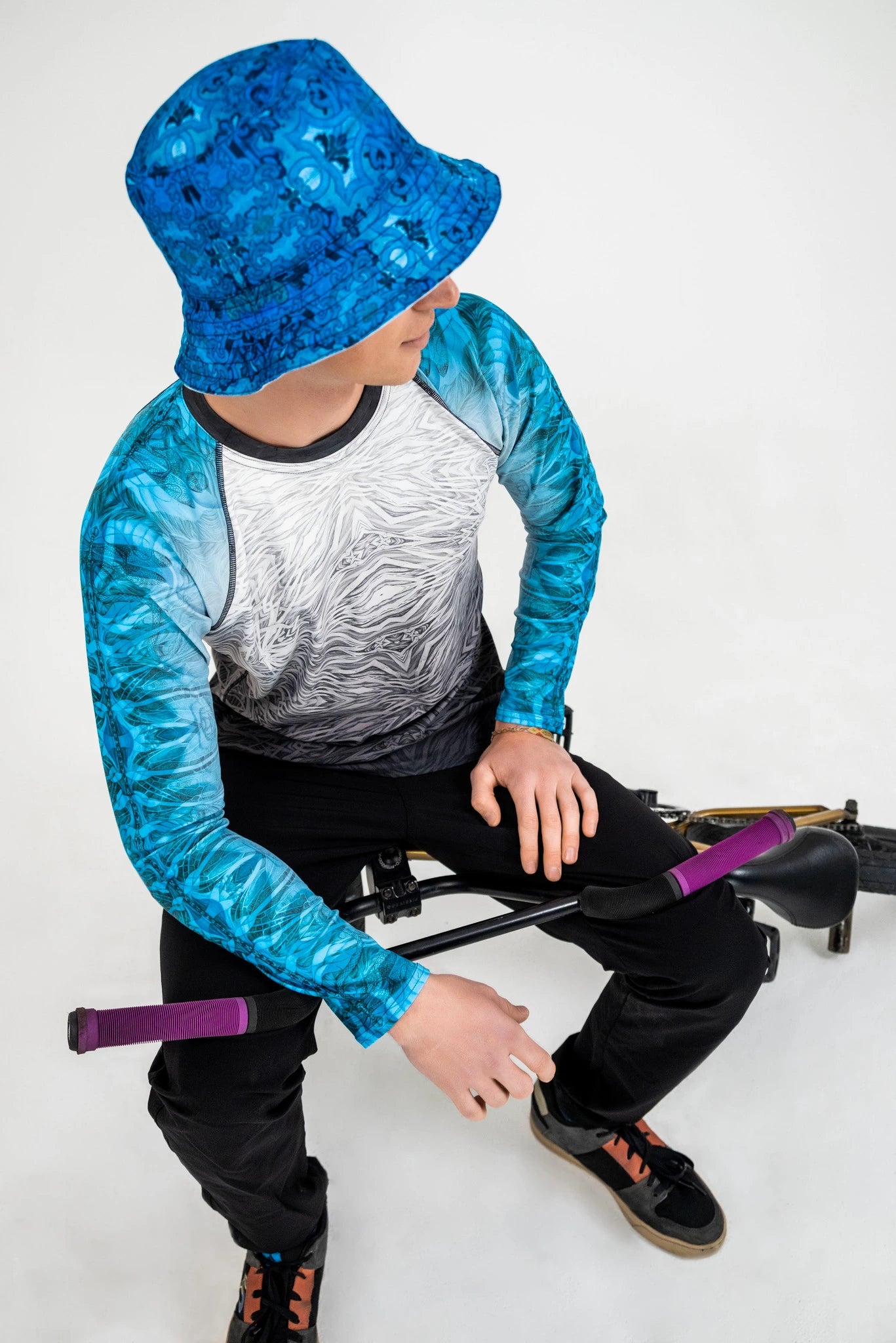Model sitting on a bike wearing a blue rash guard and bucket hat.